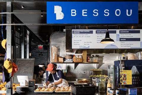 Bessou food truck interior with staff preparing food, featuring the Bessou logo on a blue sign.