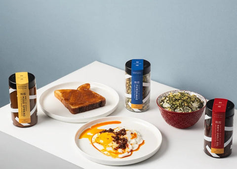 Assorted food items including toast, a bowl of salad, and packaged products on a white surface with a light blue background.